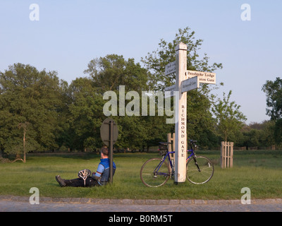 Ciclista rilassa appoggiando contro un cartello vicino al Richmond Gate nel Parco di Richmond, Surrey. Regno Unito Foto Stock
