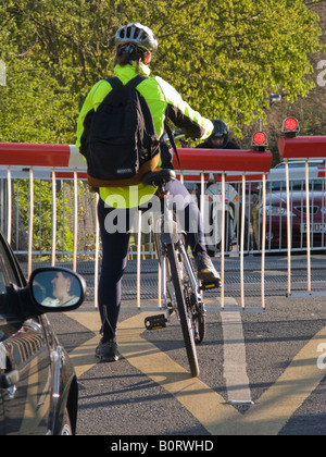 Ciclista indossando GIUBBETTO ALTA VISIBILITA in attesa presso un passaggio a livello ferroviario mentre la barriera è giù per il passaggio di un treno. Foto Stock