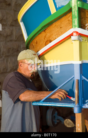 Tradizionale barca da pesca maltese; pescatore che ripulisce un occhio Luzzu di Horus o di Osiride sulla parte anteriore per proteggere i pescatori quando sono in mare. Foto Stock