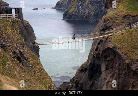 Turista femminile attraversando il carrick a rede ponte di corde sulla contea di Antrim coast Irlanda del Nord Foto Stock