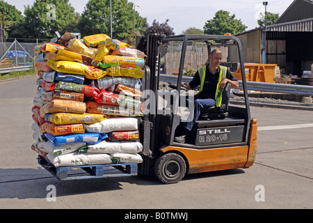 Un uomo con un carrello elevatore per spostare sacchi di compost di giardinaggio in un giardino forniture Foto Stock