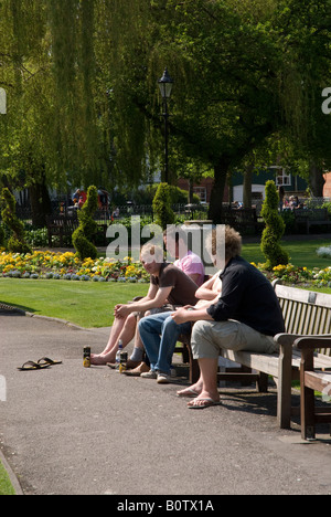 Un gruppo di giovani maschi su una panchina nel parco di bere al sole Foto Stock