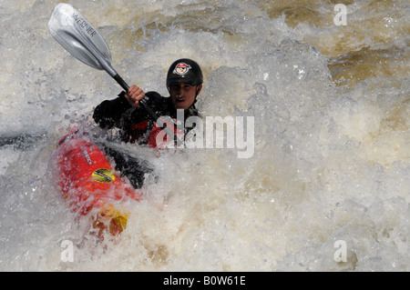 Giovane uomo in un kayak Shooting the Rapids sulle rive di un fiume Foto Stock