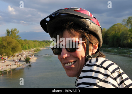 Donna che indossa gli occhiali da sole e casco per bicicletta in corrispondenza del Flaucher, una propaggine del fiume Isar, Monaco di Baviera, Baviera, Germania, Eur Foto Stock