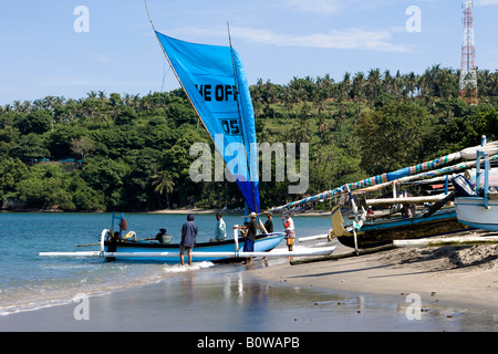 Fisherman tornando a riva dalla pesca con la vela aperta sulla sua barca outrigger, Isola di Lombok, Lesser Sunda Islands, Indone Foto Stock