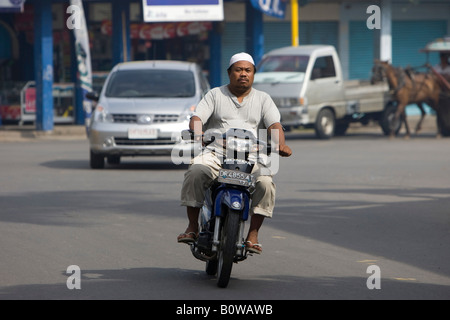 Uomo musulmano in sella ad un ciclomotore attraverso le strade della capitale Mataram, Isola di Lombok, Lesser Sunda Islands, Indonesia Foto Stock