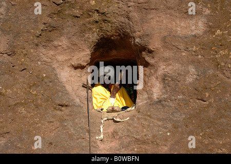 Il vecchio eremita vestito in un giallo cape pregando in una grotta piccola chiesa ricavata dalla roccia, Lalibela, Etiopia, Africa Foto Stock