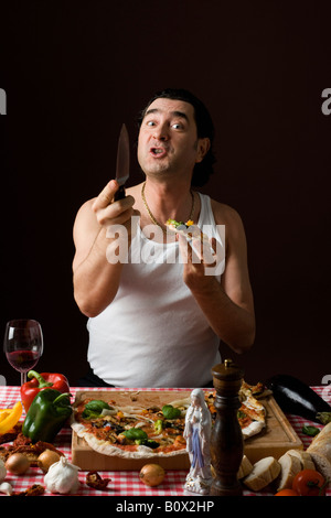 Stereotipato uomo italiano di mangiare la pizza e il possesso di un coltello in modo aggressivo Foto Stock