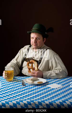 Stereotipi uomo tedesco in costume bavarese tergi bocca ad un tavolo con una birra e un pasto tedesco Foto Stock