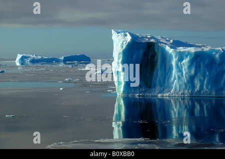 Un lato di un blu iceberg antartico nell'Oceano del Sud su un quasi piatta mare coperta da ghiaccio floes, Antartide, Oceano Meridionale Foto Stock