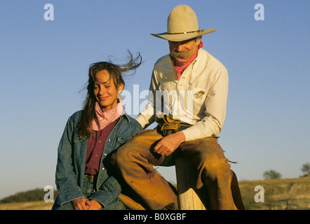 Un cowgirl ospite a dude ranch vicino a San Antonio Texas siede su un recinto con un cowboy wranger in chaps e un grande cappello al tramonto Foto Stock