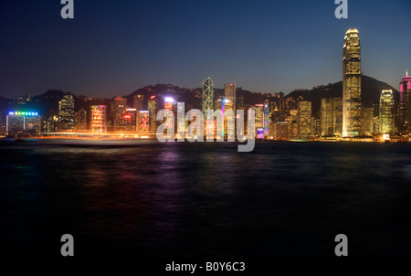 Barche di spostarsi in tutta l'acqua e di fronte all'ufficio edifici del porto di Hong Kong in Cina al crepuscolo e di notte al tramonto Foto Stock