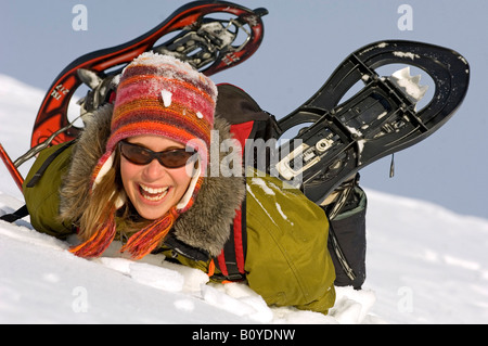 Giovane donna bionda con le racchette da neve, giacente nella neve, Francia, Alpi Foto Stock