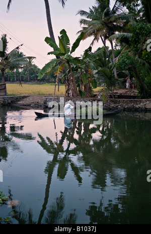 INDIA Kerala agricoltore indiano con una barca a remi pieno di erba che egli è il canottaggio lungo i canali nelle lagune del Kerala al tramonto Foto Stock