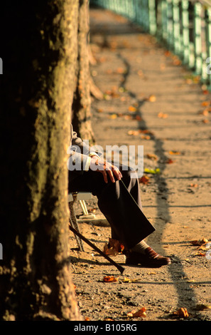 Uomo vecchio con un bastone da passeggio seduta su una panchina nel parco nella luce della sera Foto Stock