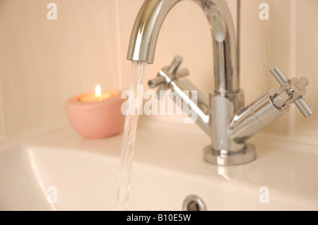 Toccare in esecuzione nel lavandino con candela in background Foto Stock