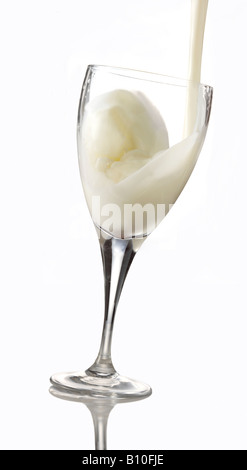 Il latte che viene versato in un bicchiere contro uno sfondo bianco Foto Stock