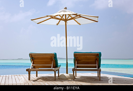 Sedie a sdraio che si affaccia sulla piscina infinity e laguna a Anantara resort nelle Maldive Foto Stock