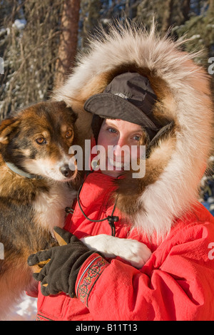 Dogsled musher Julie Estey tenendo premuto uno dei suoi cani racing e vestito di parka che indossava in Yukon Quest 1.000 miglio dogsl Foto Stock