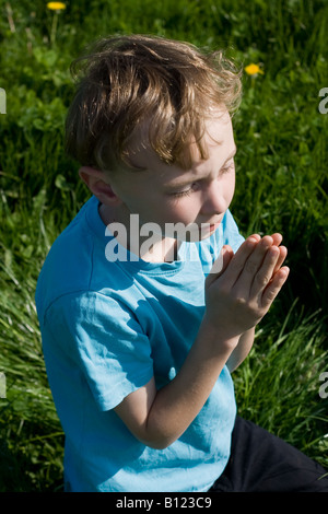 Giovane ragazzo che prega nel campo Foto Stock