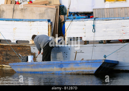 Uomo in un punt la verniciatura dello scafo di un piccolo peschereccio in legno barca Foto Stock
