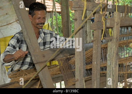 Uomo che utilizza la fibra di cocco twin sul telaio la produzione di fibre di cocco zerbini in casa cottage industry Kerala India Foto Stock