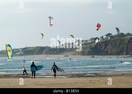 Kitesurfers sull'acqua e surfisti che camminano con le loro tavole sulla spiaggia in un giorno di inverni, Bantham, Devon. REGNO UNITO Foto Stock