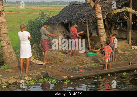 Famiglia di pescatori riassettavano le reti al fianco di canale in lagune del Kerala India le risaie nel retro Foto Stock