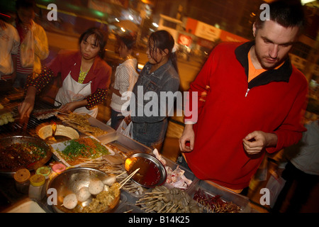 Un uomo occidentale acquisto barbeque da una bancarella di strada in Cina Foto Stock