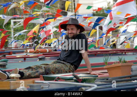 Uomo in cappello da cowboy rilassante sulla sua narrowboat circondato da bandiere e bandierine al Canalway Cavalcata, Little Venice, Londra Foto Stock