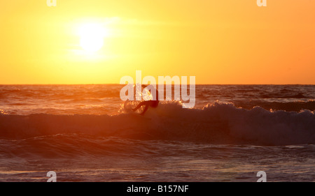 Un surfista Cavalca le onde della sera come il sole tramonta su Sennen beace in Corwall, UK. Foto Stock