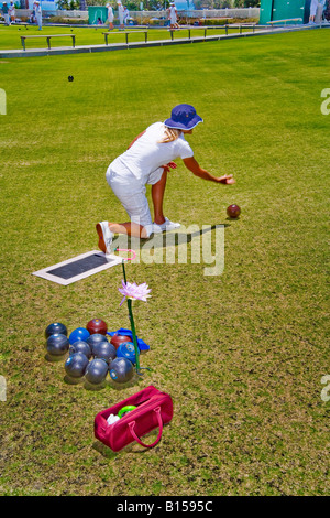 Indossando il regolamento bianco uniforme una giovane donna rotoli un vaso palla durante un prato bowling concorrenza in Laguna Beach CA Foto Stock