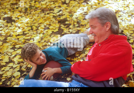Padre e figlio rilassarsi in foglie di autunno dopo la riproduzione di cattura con un calcio americano. Foto Stock