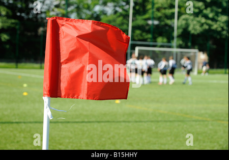 Una luminosa bandiera rossa sventolata in primo piano con sfocate giocatori di calcio in background sul tappeto erboso artificiale di calcio. Foto Stock