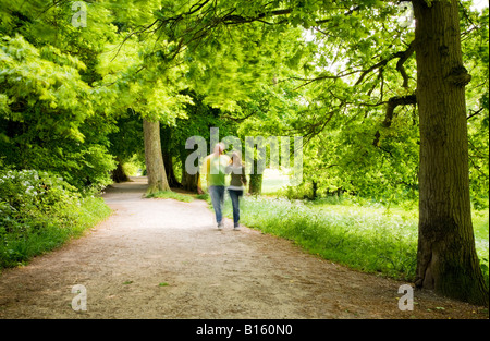 Giovane camminando sotto braccio lungo un sentiero frondoso in pezzata sole estivo a Coate Water Country Park, Wiltshire, Inghilterra, Regno Unito Foto Stock