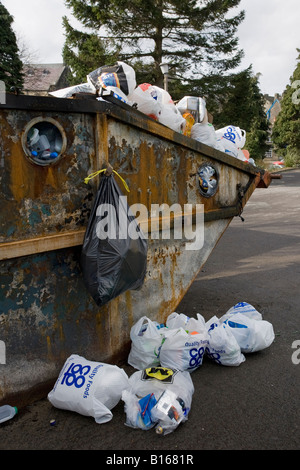 Skip di riciclaggio sovraccarico, pieno in alto (rifiuti e rifiuti gettati via, sacchi di plastica che si gettano via terra, problema di rifiuti) - Baildon, Yorkshire, Inghilterra UK. Foto Stock