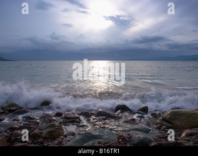Tranquillo paesaggio marino al tramonto mostra piccole onde e rocce Foto Stock