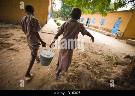 I bambini portano un secchio di acqua al Nyassia scuola elementare nel villaggio di Nyassia Senegal Foto Stock