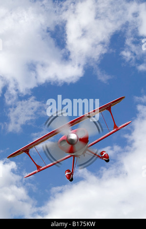 Un biplano rosso battenti in un blu cielo nuvoloso Foto Stock