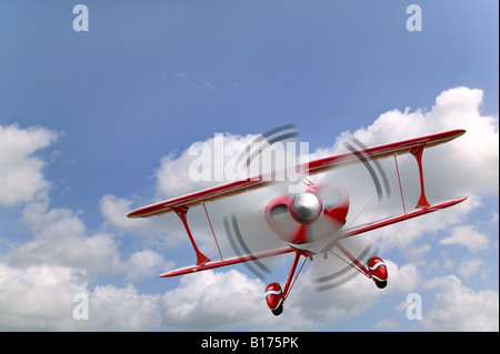 Un biplano rosso battenti in un blu cielo nuvoloso Foto Stock