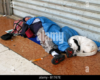 Un senzatetto e il suo cane dormire accanto a un otturatore in una trafficata via dello shopping di Milano, Italia, UE Foto Stock