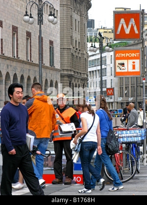 Un uomo in un giubbotto arancione mani giornali gratuiti come persone inserire linee della metropolitana milanese Foto Stock
