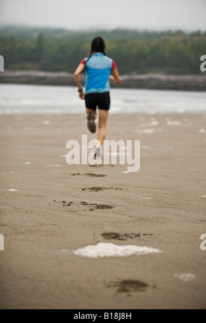 Una giovane donna che corre lungo le rive della spiaggia di Mispec Park, San Giovanni, New Brunswick, Canada. Foto Stock