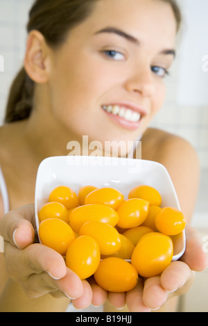 Giovane donna tenendo fuori la vaschetta del giallo di pomodori ciliegini Foto Stock