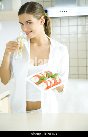 Giovane donna azienda pomodoro e mozzarella insalata, odore di condimento per insalata Foto Stock