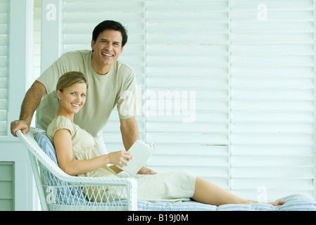 Coppia insieme sul patio, sorridente in telecamera, donna azienda prenota Foto Stock