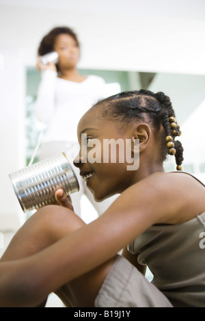 Ragazza parla nel barattolo di latta telefono, madre in ascolto in background Foto Stock