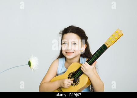 Bambina suonare la chitarra giocattolo, accanto al fiore Foto Stock