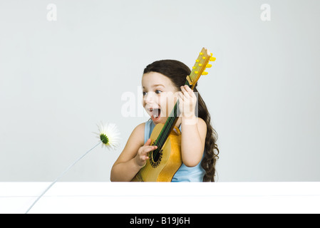 Bambina suonando la chitarra, rendendo faccia come fiore si inclina verso di lei Foto Stock