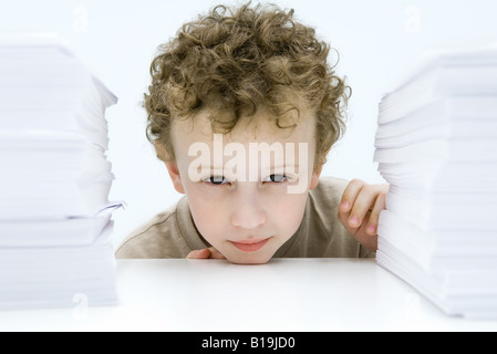 Capelli ricci boy accordi di peering tra pile di carta, sorridente in telecamera Foto Stock